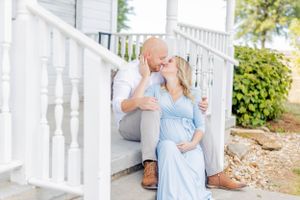A couple in romantic embrace sits on white porch stairs during a maternity photo session in Springfield, Missouri.
