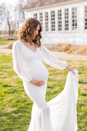 Woman in white maternity dress poses gracefully on lawn with flowing fabric in Springfield, Missouri.