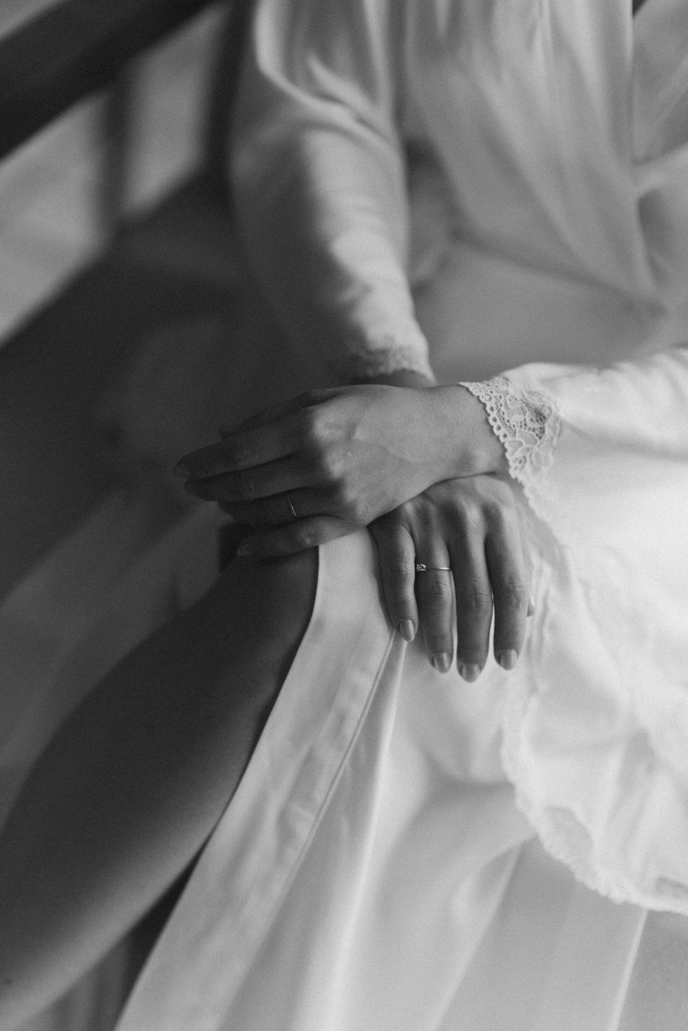 A delicate black and white photograph showing hands with lace sleeves and a wedding dress.