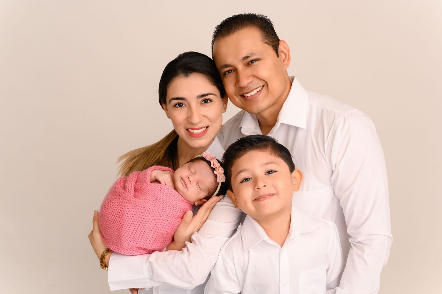 Happy family portrait session in studio with warm lighting and white background.