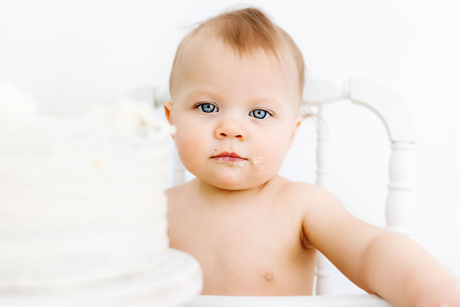 Small infant in a white setting looks at camera with bright blue eyes and delicate features.