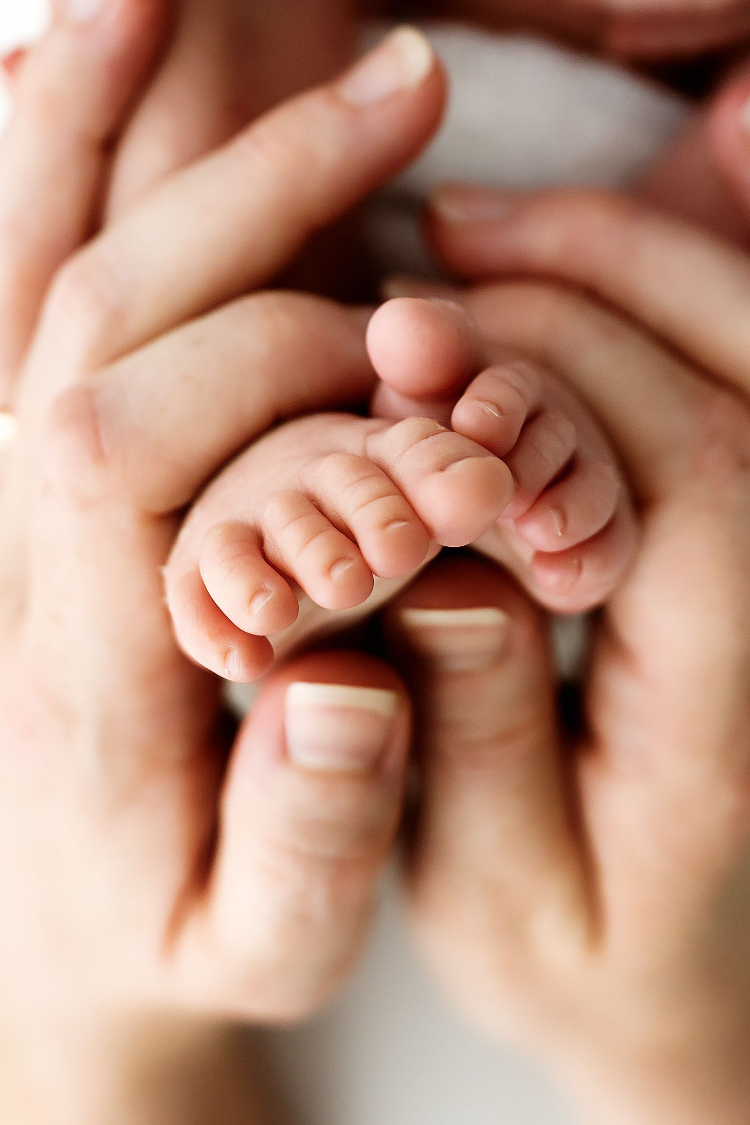 A close-up macro photo of a baby's tiny fingers being gently held by adult hands against a soft blurred background.