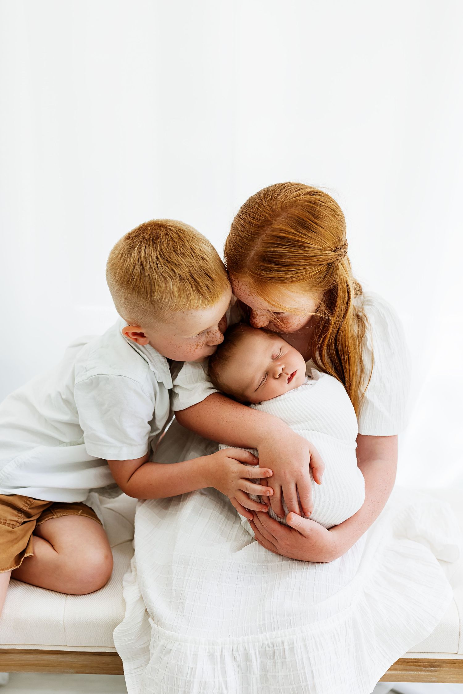 Series of tender sibling moments showing a child kissing a sibling's head on white bedding in three progressive shots.