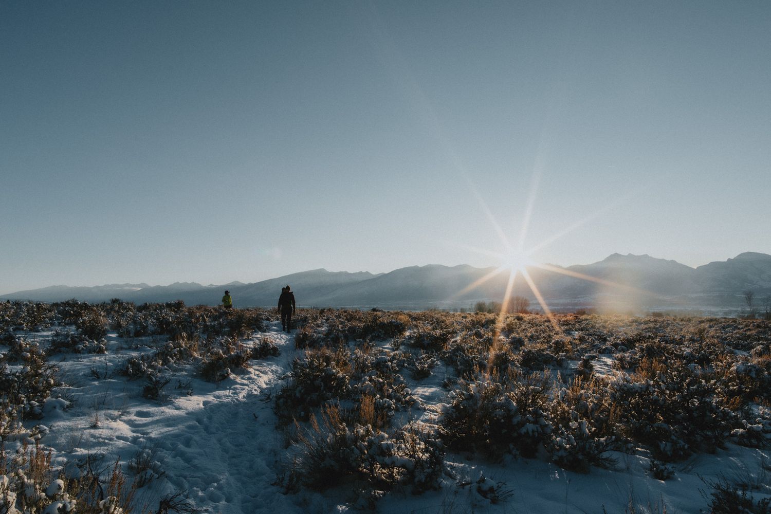 Hikers on a winter day, with the sun setting over the mountains in the Bitterroot Valley.