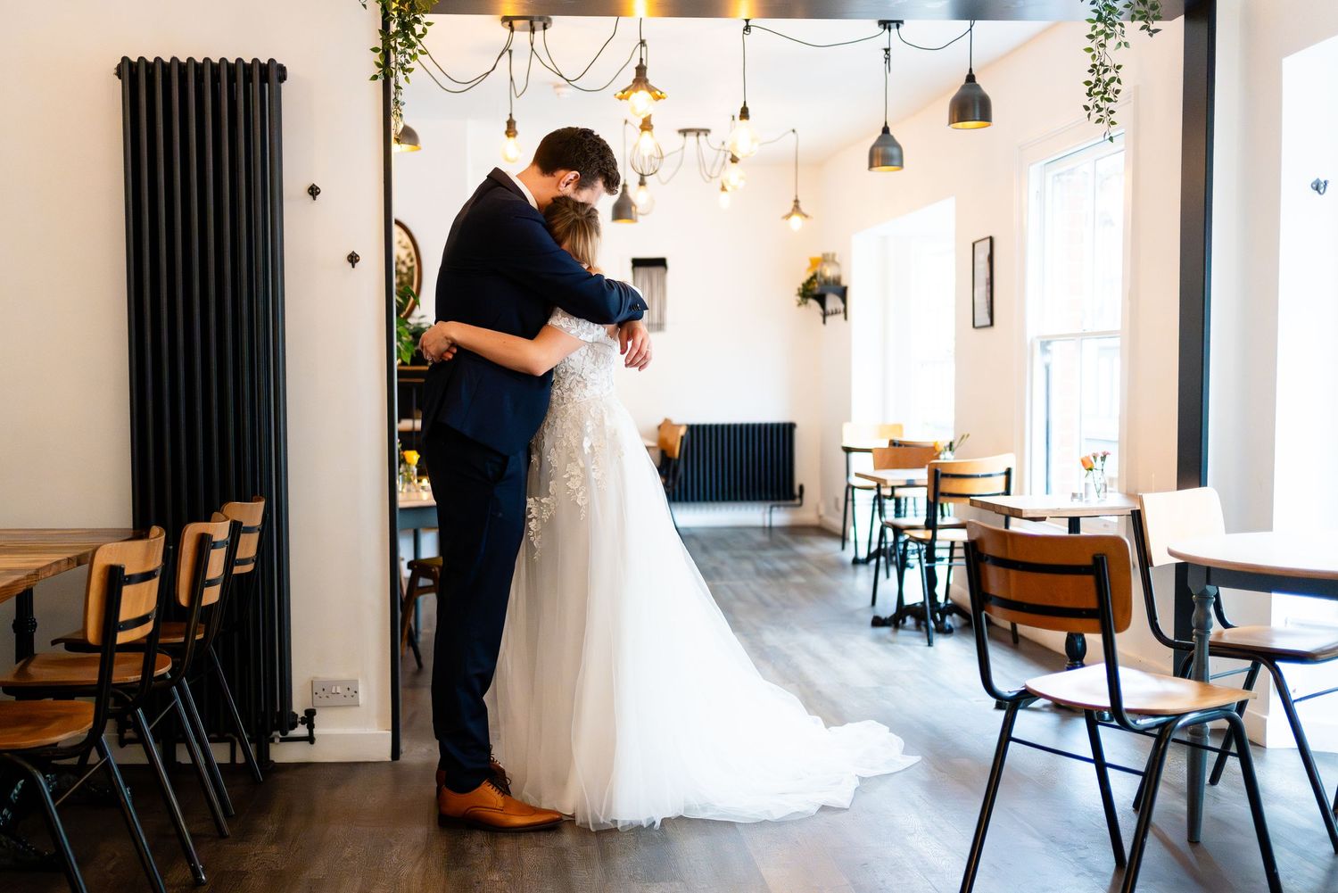 Two people sharing an intimate moment in a modern cafe interior with white walls and pendant lighting.