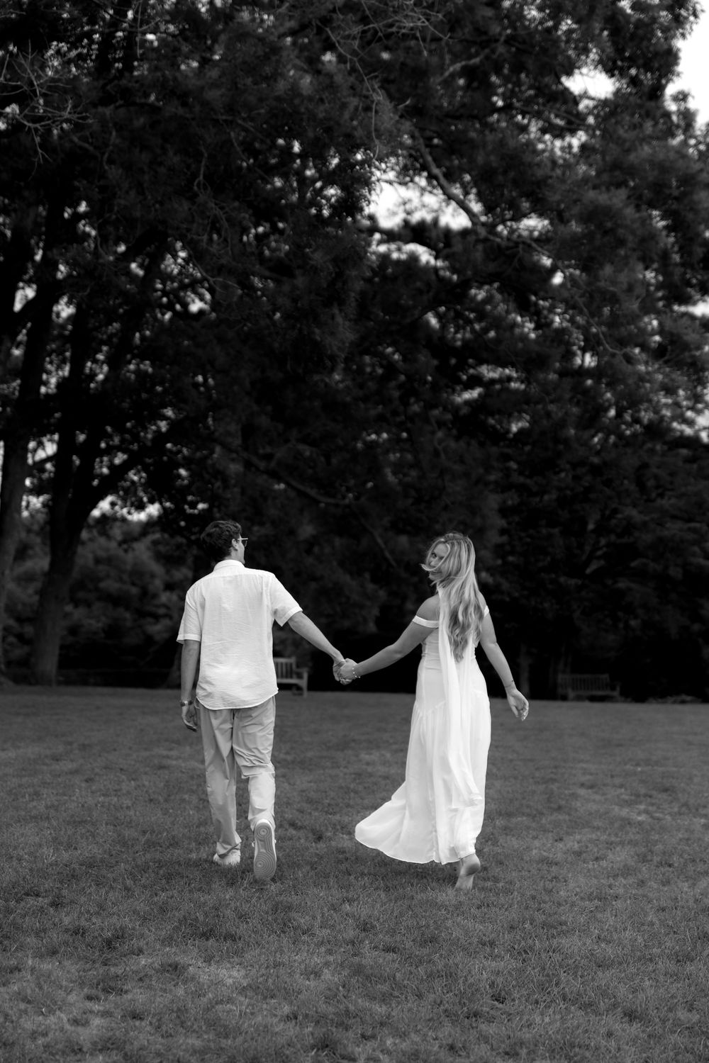 Black and white photo of two people walking on a grassy hill with trees behind them.
