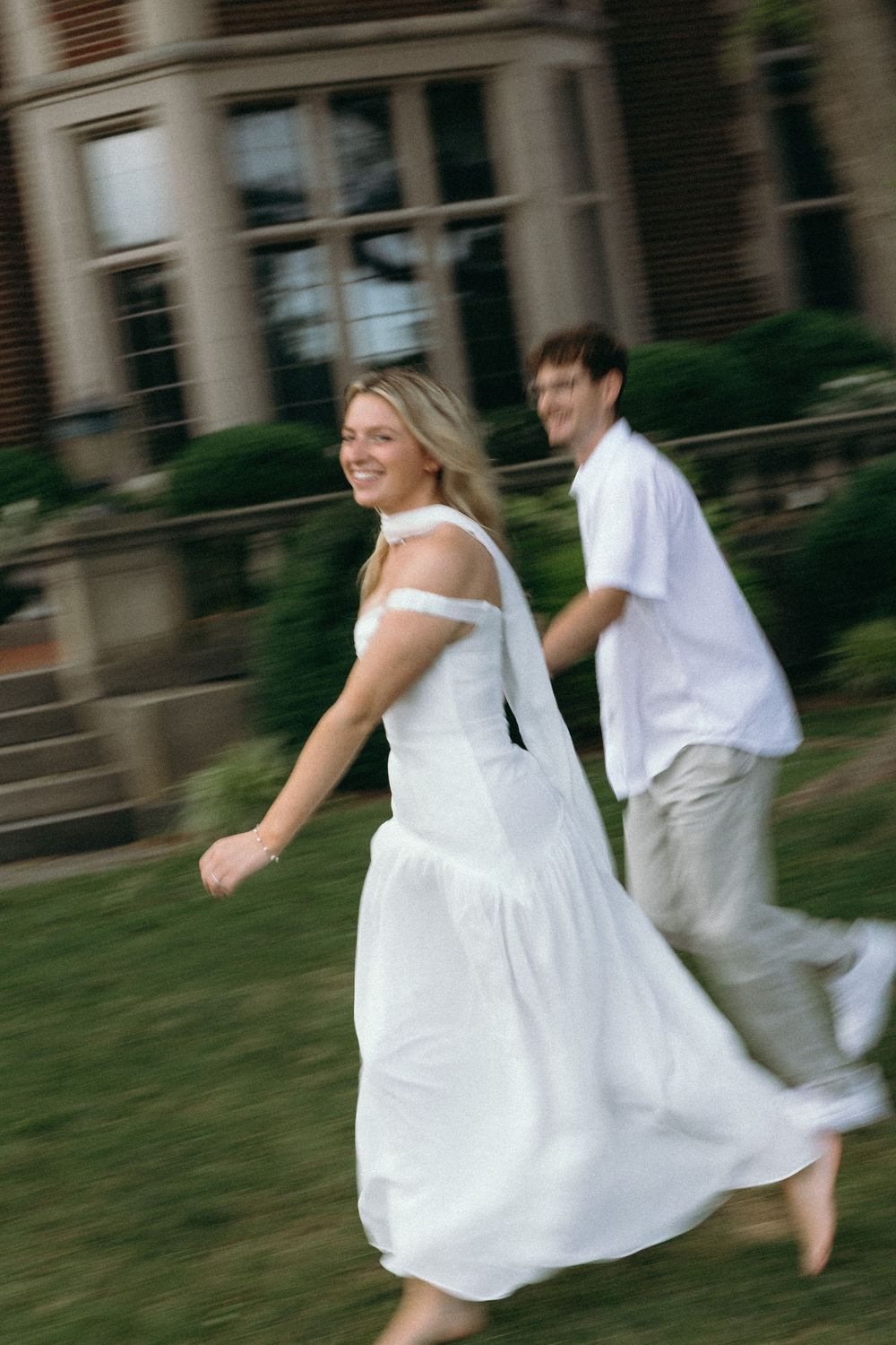 Motion-blurred shot of two people in white clothing running playfully outdoors.