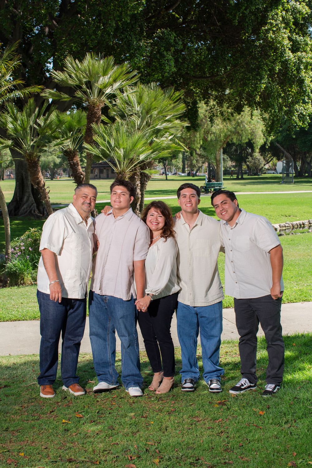 People in coordinated casual outfits stand together on grass with palm trees in the background.