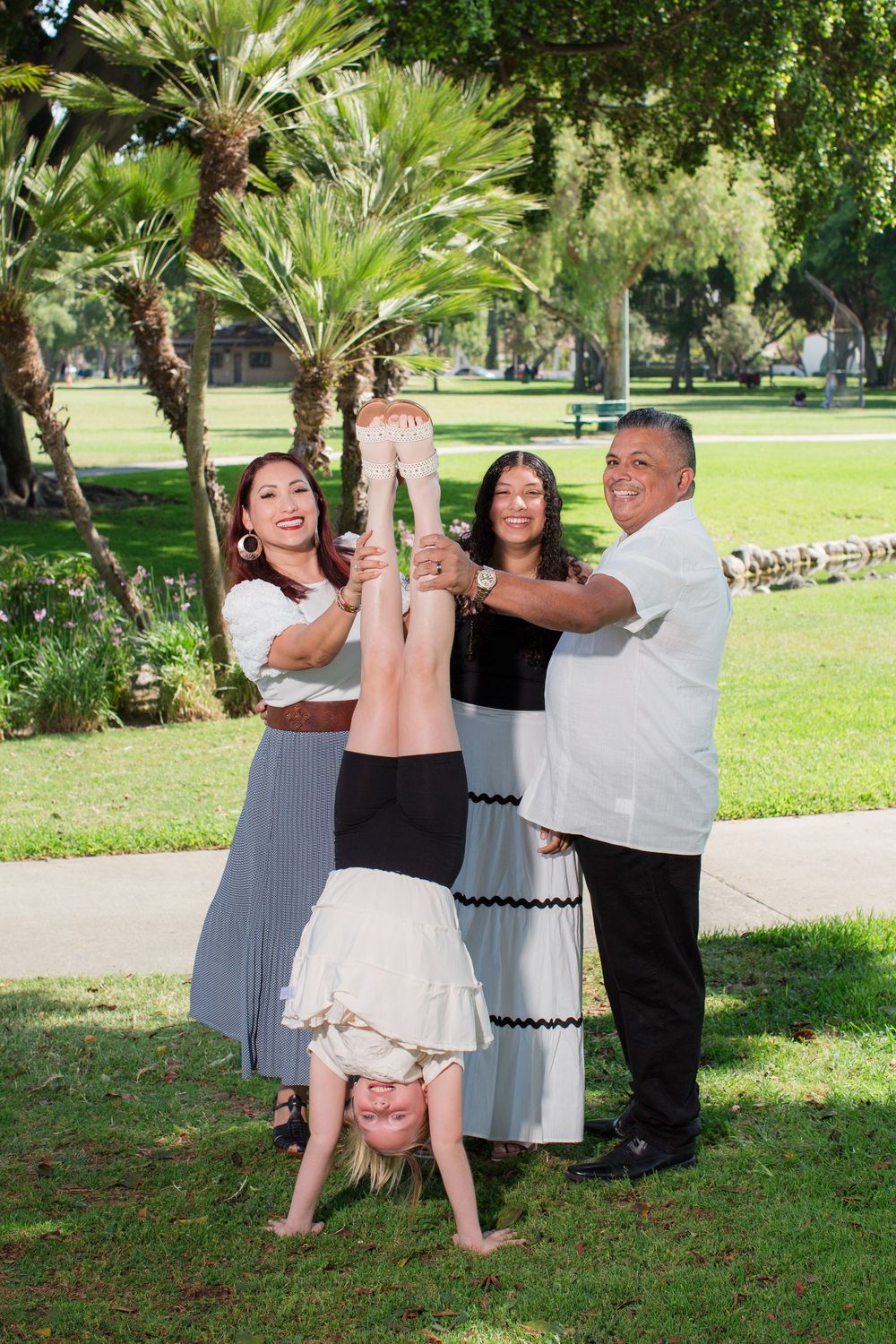 Couples dancing in casual attire on a grassy lawn surrounded by palm trees.