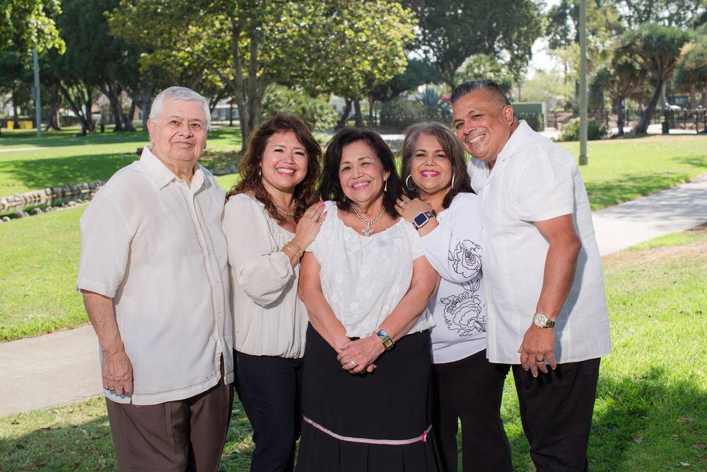 A group poses together outdoors in matching white shirts and jeans on a sunny day in a park.