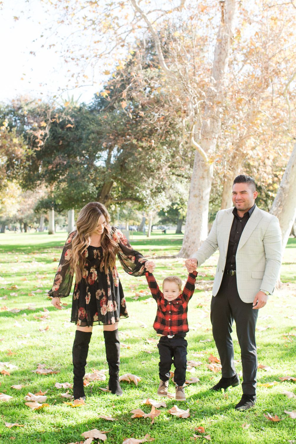 Family walking together through park with sycamore trees and green grass.