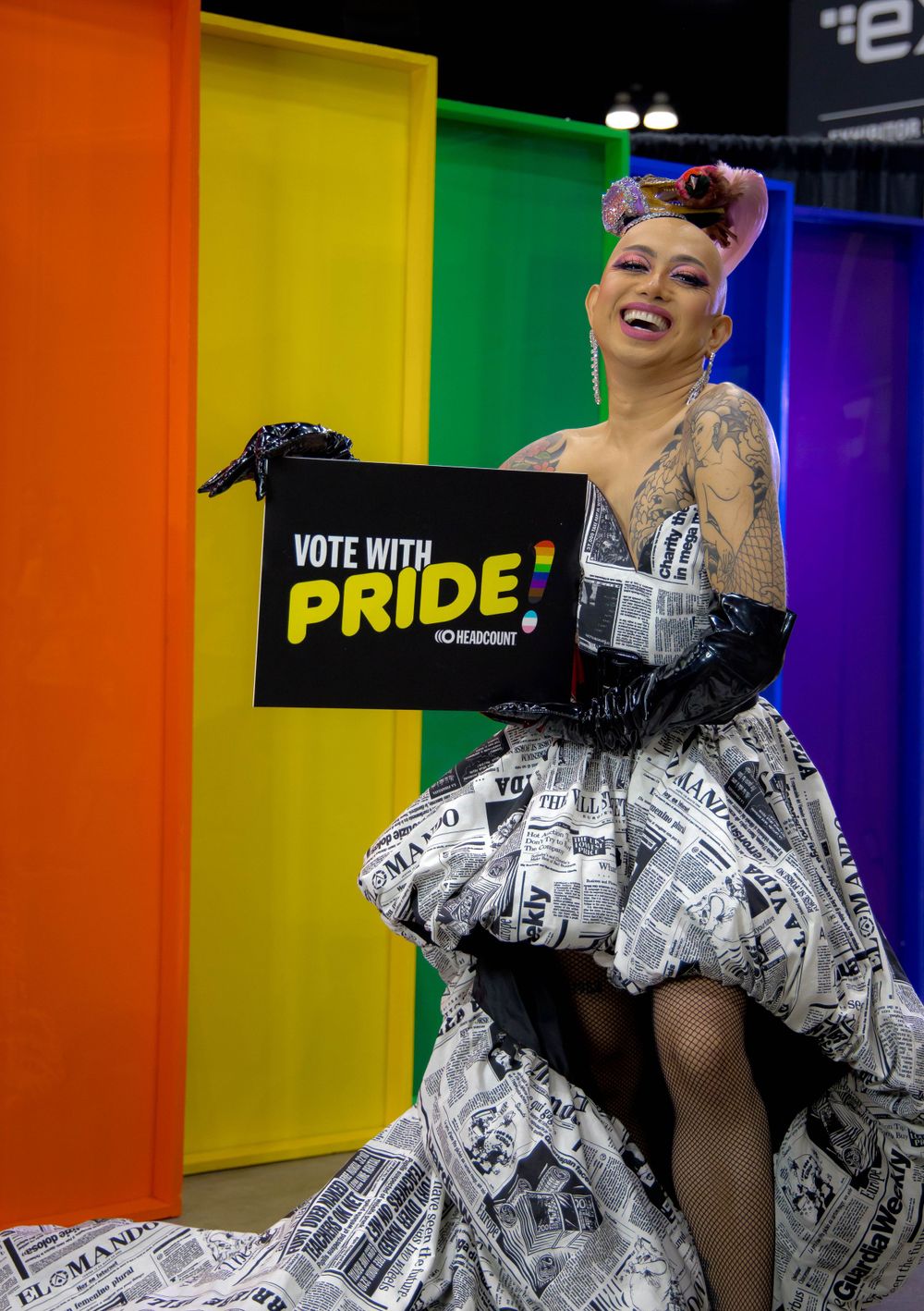Ongina at dragcon in front of rainbow with a sign that says "Vote with pride!"