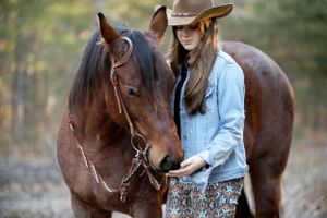 young woman standing next to a horse that is sniffing her hand