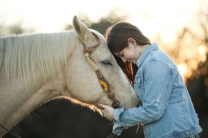 young woman with her forehead pressed against her horse's head