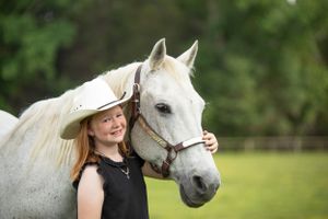 young girl wearing a cowboy hat standing next to a grey horse