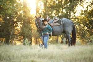 girl standing next to blue roan horse with sunshine coming through the trees behind them, Forney, Texas