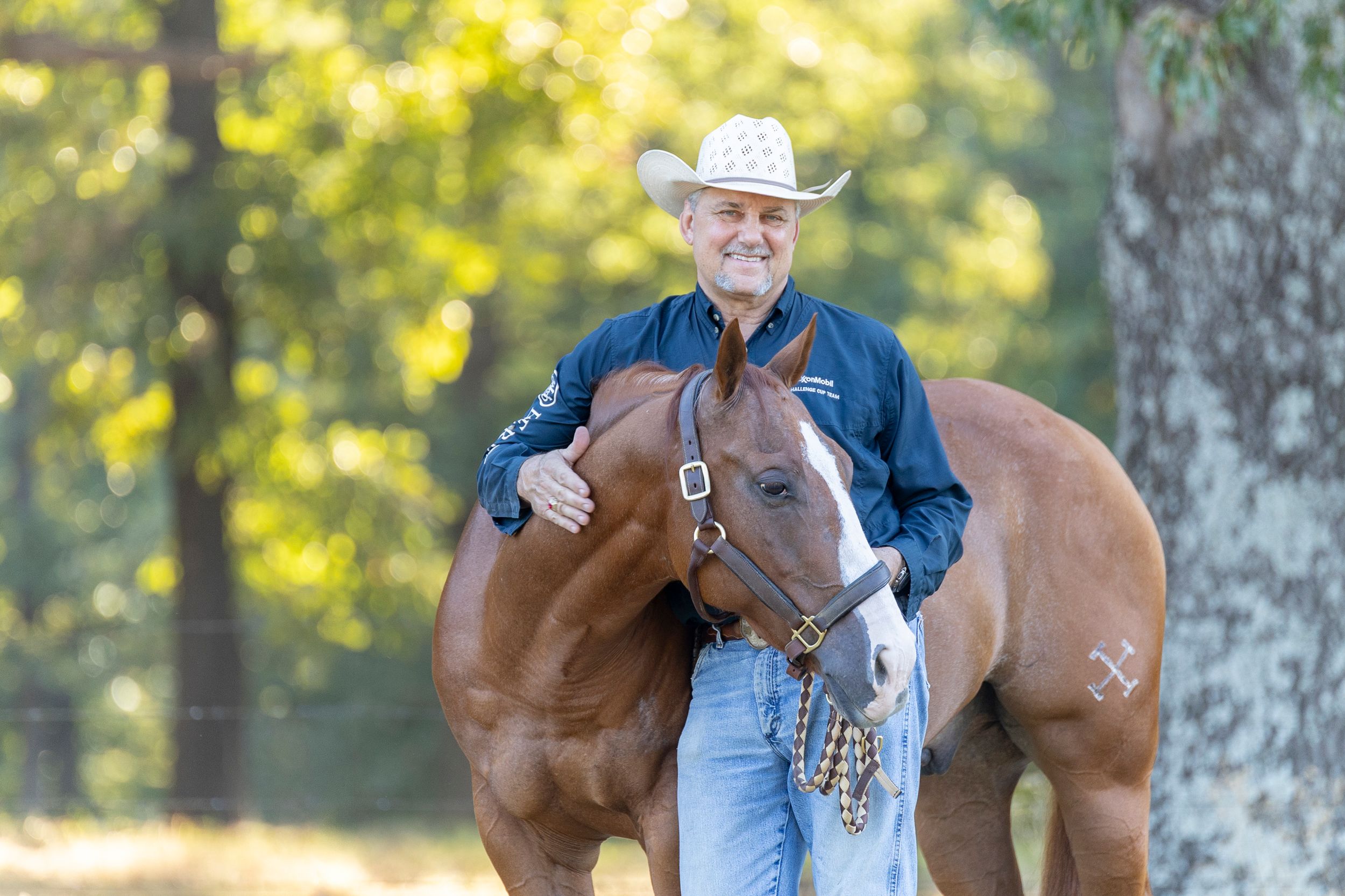 Man standing with his arm around his horse, smiling at the camera.