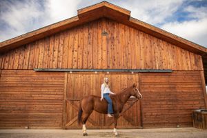 girl sitting horseback in front of wooden barn, equestrian senior portraits