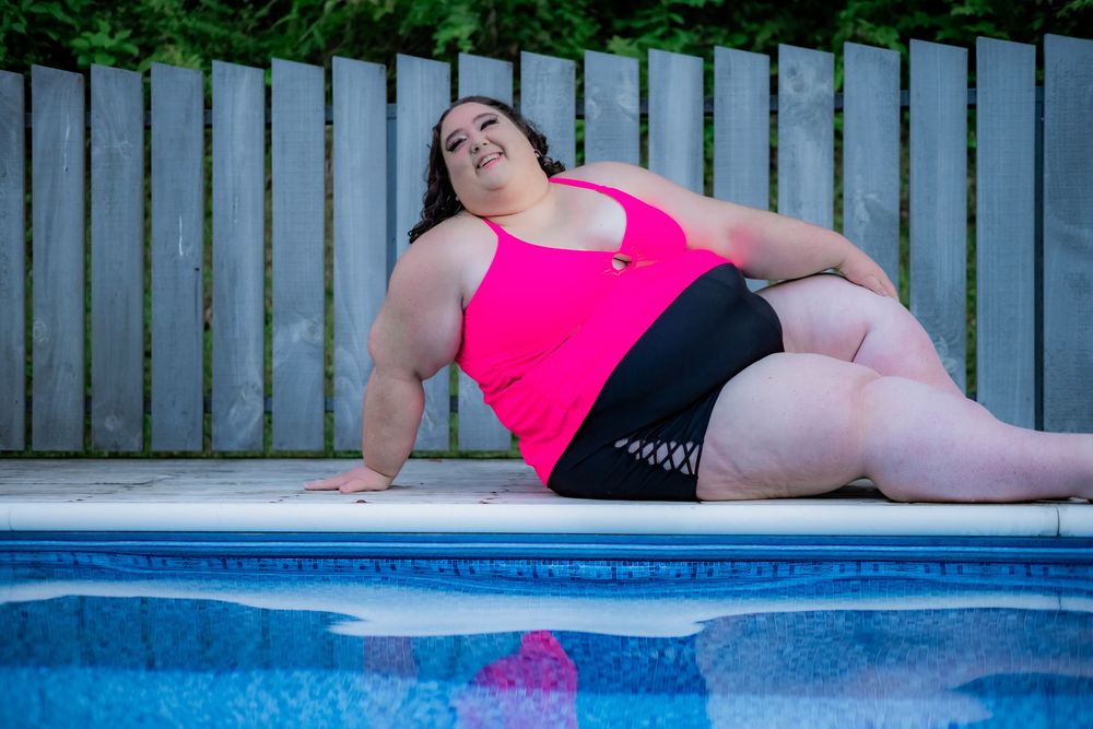Plus-size woman in pink tankini relaxing by outdoor swimming pool on sunny day. Pool Boudoir. Poolside Boudoir.