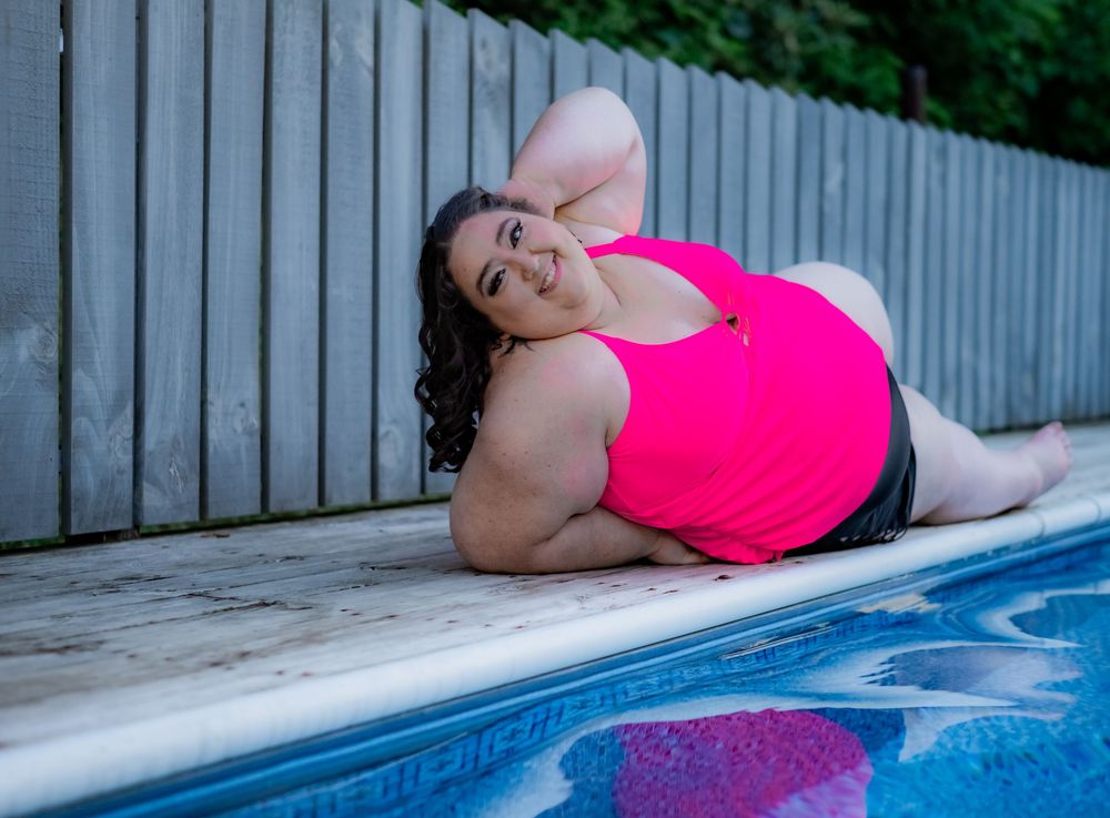 Plus-size woman in pink swimsuit posing by a backyard pool on a sunny day. Pool Boudoir. Poolside Boudoir.