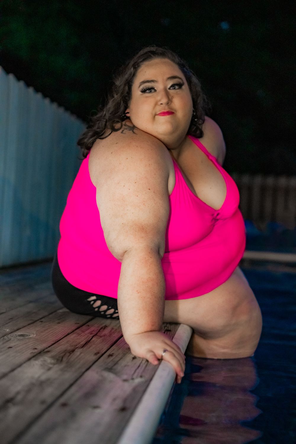 Plus-size woman in pink bikini top posing poolside on wooden deck at dusk. Pool Boudoir. Poolside Boudoir.