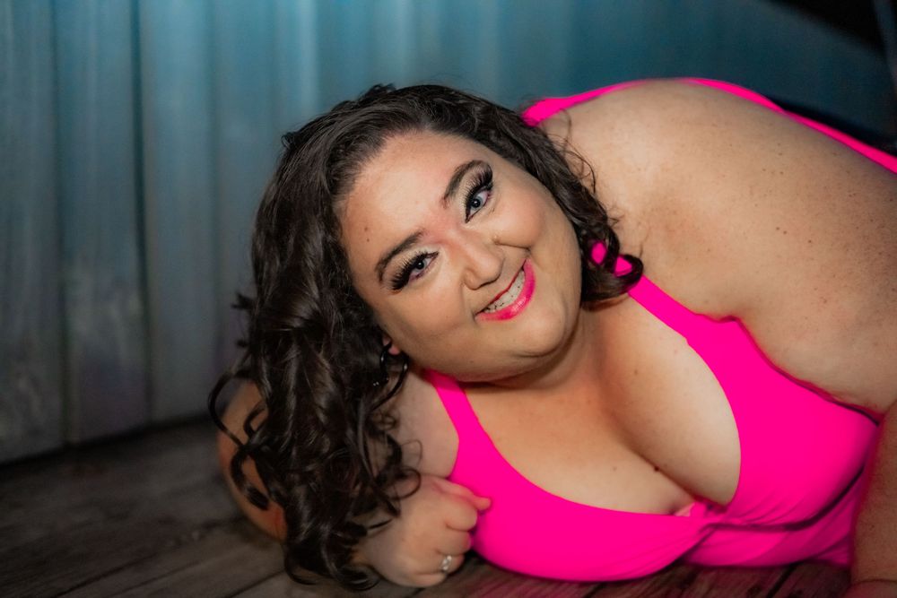 Woman in pink bikini top posing with curly dark hair and bold makeup under studio lighting. Pool Boudoir. Poolside Boudoir.