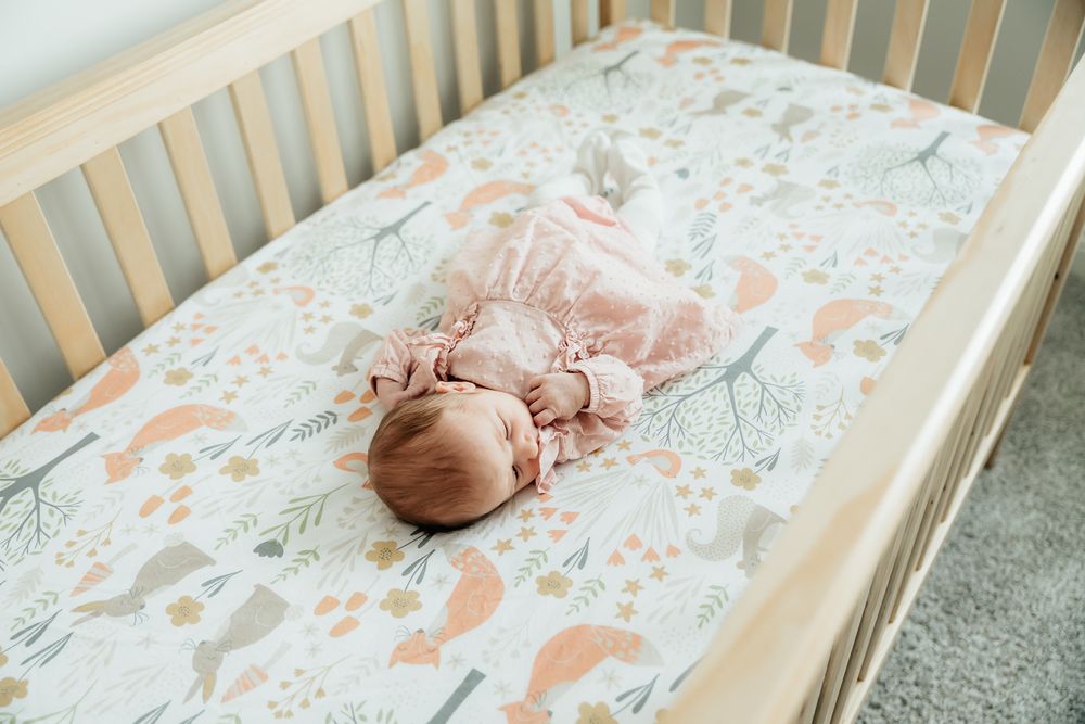 A baby sleeping peacefully in a wooden crib with floral bedding and plush toys.