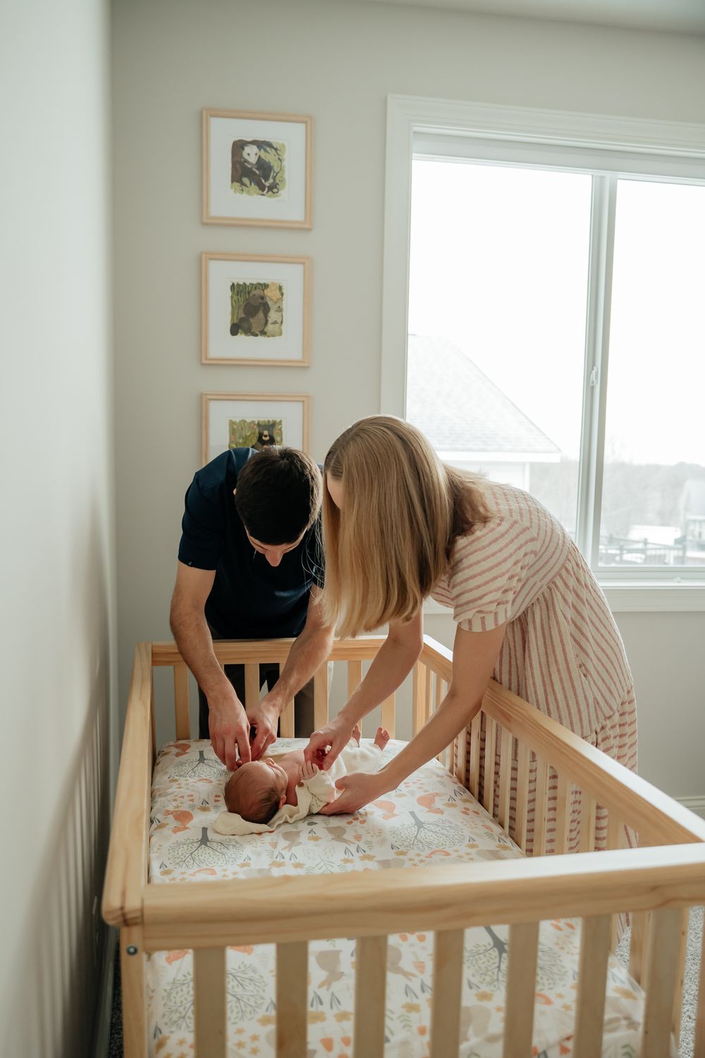 Parents changing their newborn's diaper on a floral-patterned changing pad in a nursery with framed art.
