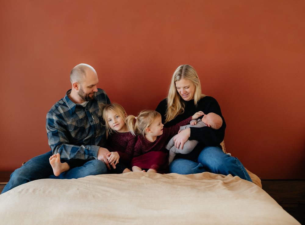 Family with children relaxing together on bed against terracotta colored wall.