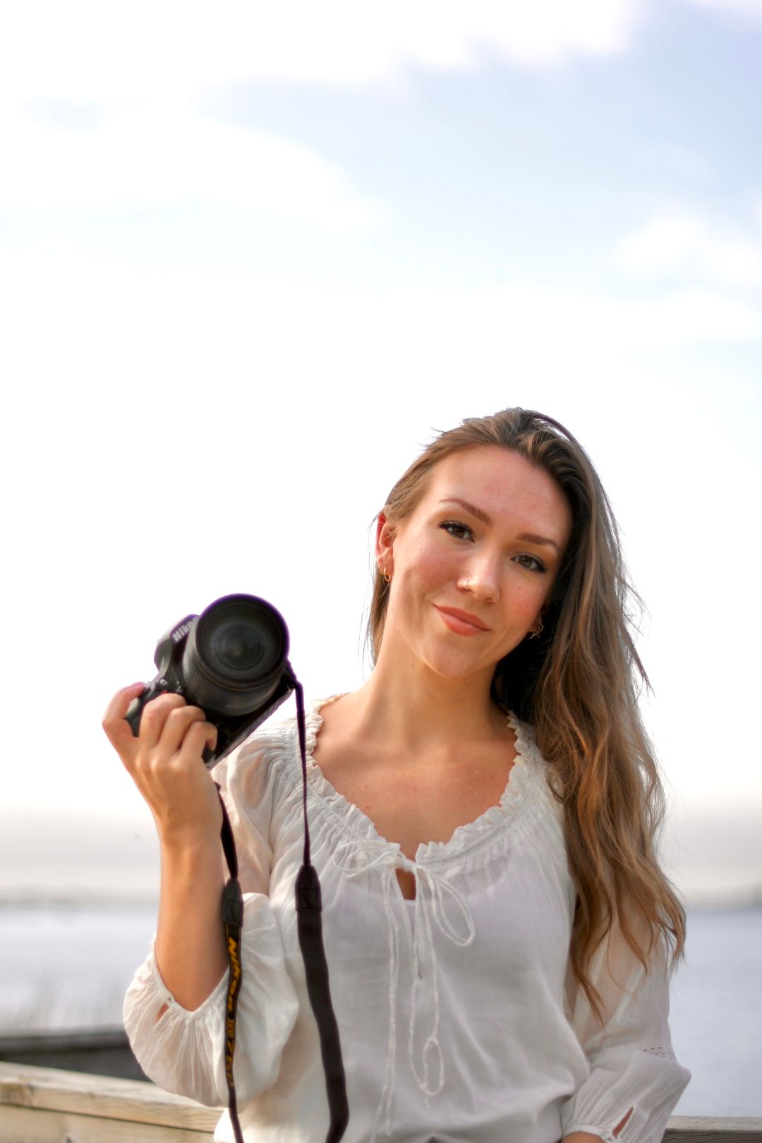 Portrait of photographer holding professional camera in white blouse at beach.