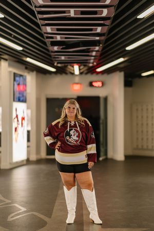 A figure wearing a Florida State Seminoles hockey jersey and white boots poses in an indoor hallway with fluorescent lighting.