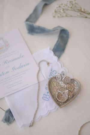 Vintage silver heart locket on a chain next to a wedding invitation and blue velvet ribbon with baby's breath flowers.