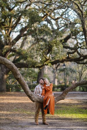 Scenic outdoor portrait showing loving couple nestled among majestic oak tree branches in a serene park setting.