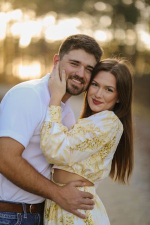 Romantic outdoor portrait of couple embracing at sunset with golden bokeh lighting in background.