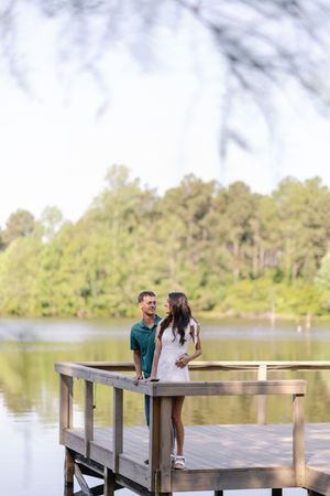 Couple standing on a wooden dock by a serene lake surrounded by lush green trees.