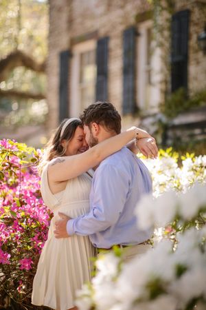 A romantic couple embraces in a garden with blooming pink azaleas and white flowers on a sunny spring day.