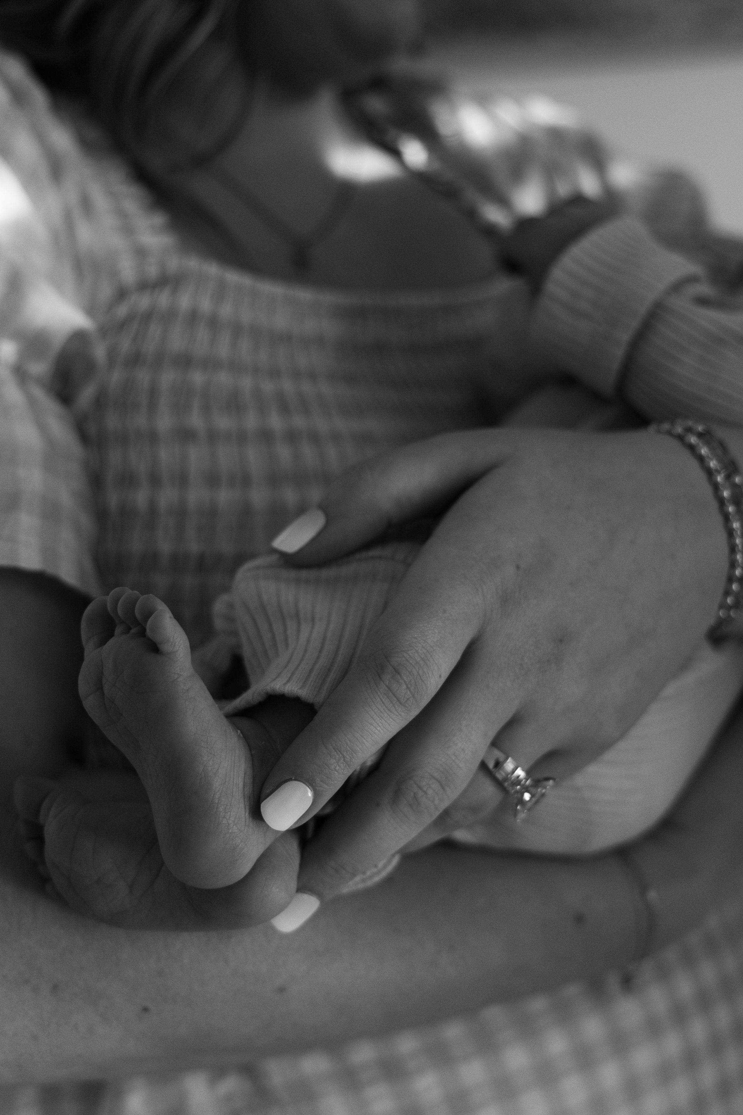 Black and white photo of a mother cradling her newborn baby's tiny feet in her hands, wearing a wedding ring.