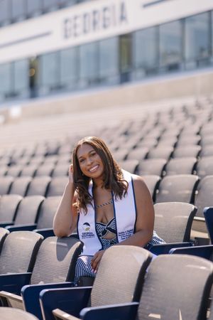Smiling graduate poses in stadium seating wearing a Georgia graduation stole at University of Georgia.