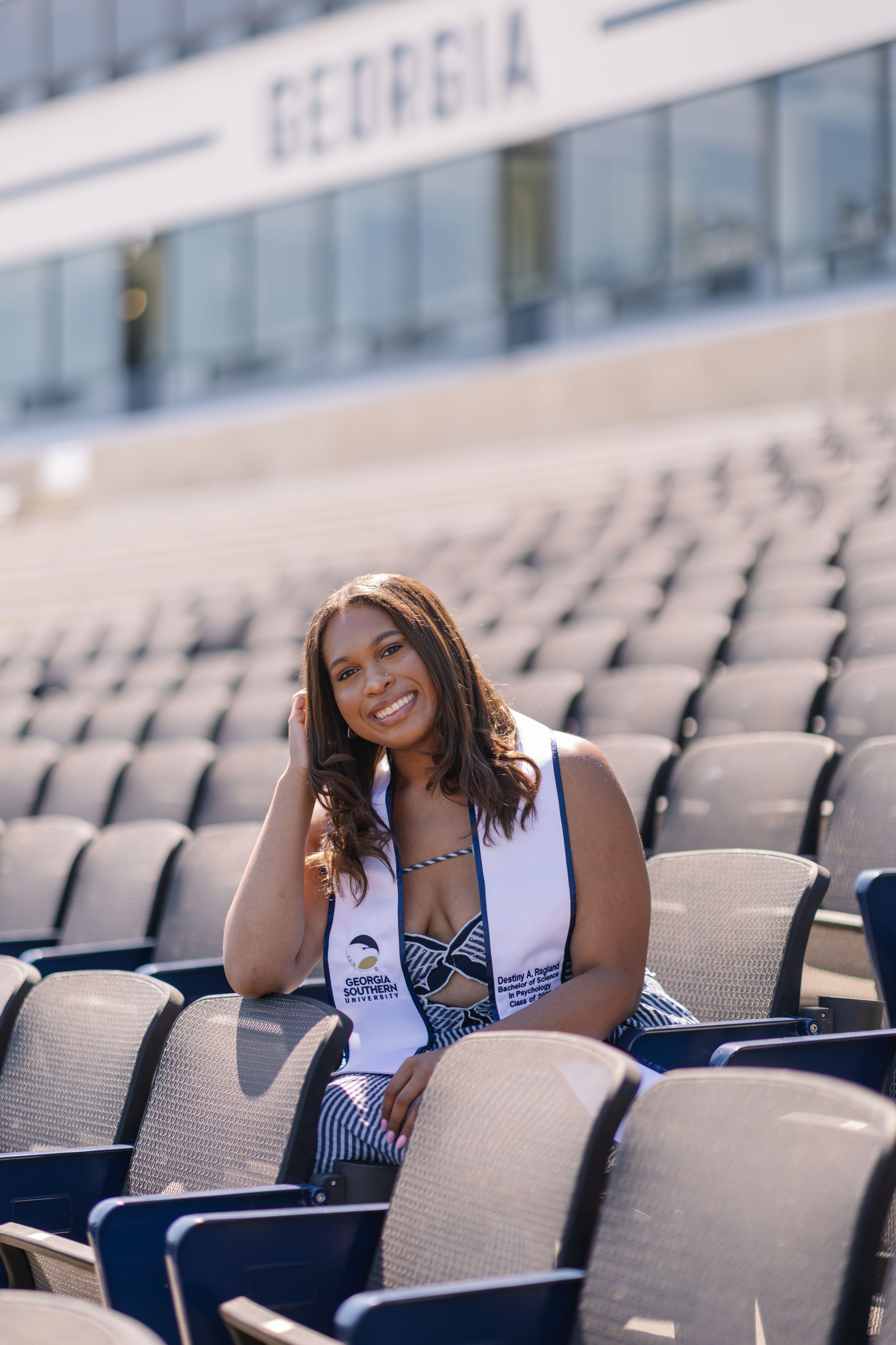 Smiling graduate poses in stadium seating wearing a Georgia graduation stole at University of Georgia.