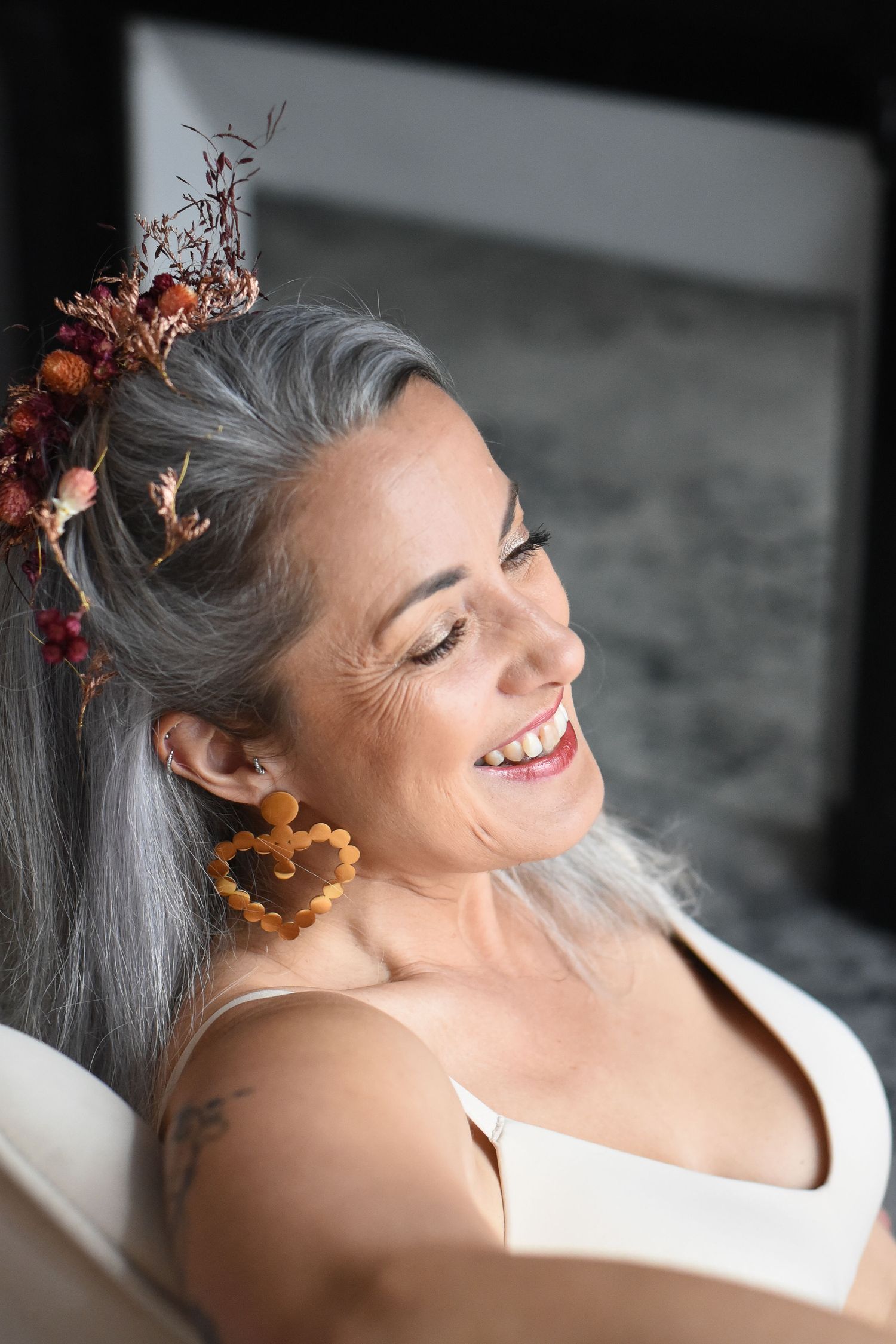 A person with silver hair smiles while wearing autumn-colored flowers in a black and white selective color photo series.