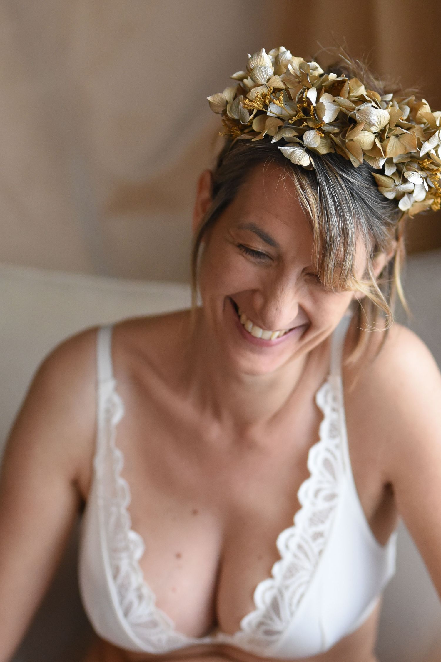 Woman wearing white lingerie and gold leaf crown laughs joyfully in intimate boudoir portrait series.