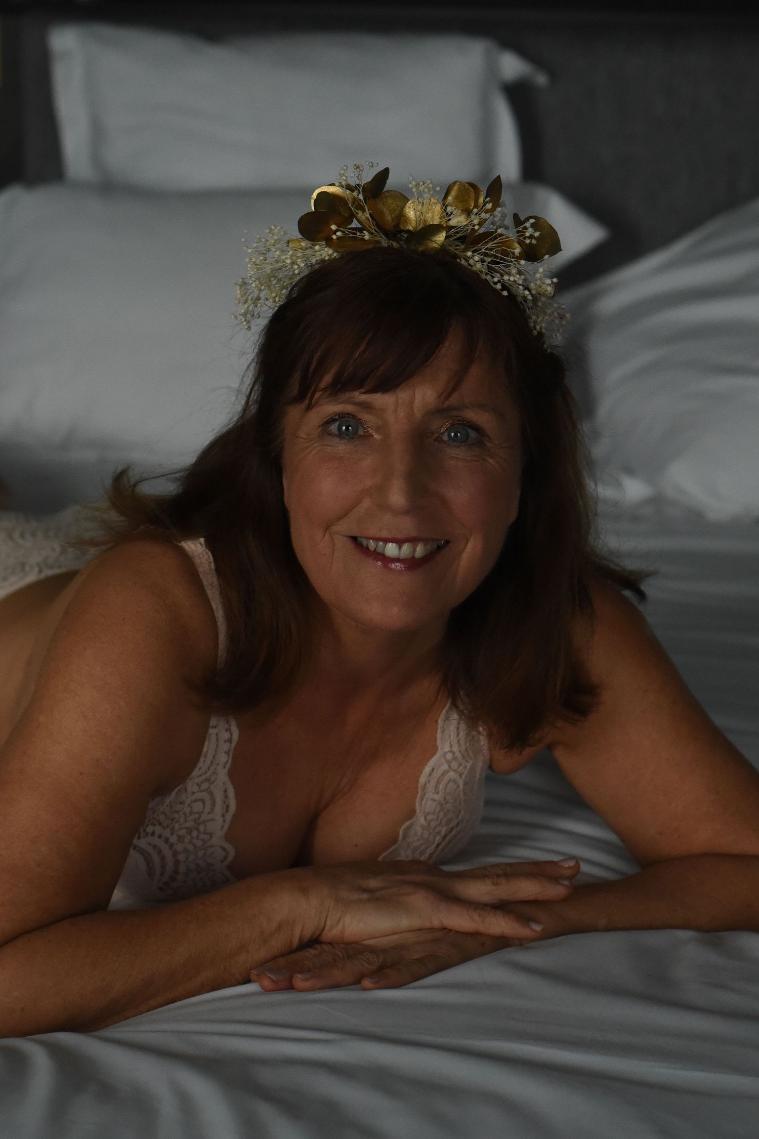 Person wearing a golden crown lying on white bedding in a boudoir photography setting.