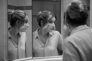 Black and white photo of woman examining her reflection in a bathroom mirror before wedding ceremony.