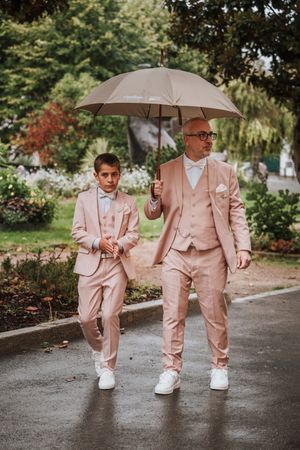 Man and boy in matching pink suits walking under umbrella in rain.