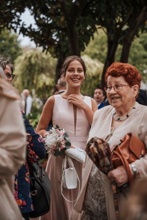Smiling bridesmaid in pink dress holding a floral bouquet at an outdoor wedding ceremony.