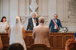 A wedding ceremony in a formal hall with a bride, groom, and officiant at a decorated podium.