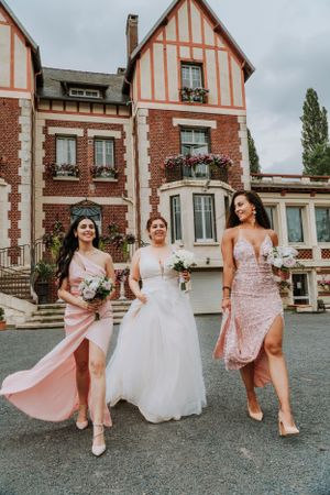 Wedding party members in pink dresses and white gown walking outside a Tudor-style mansion.