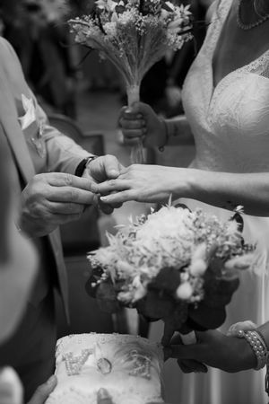 Black and white photo of a groom placing a wedding ring on the brides finger during the ceremony.