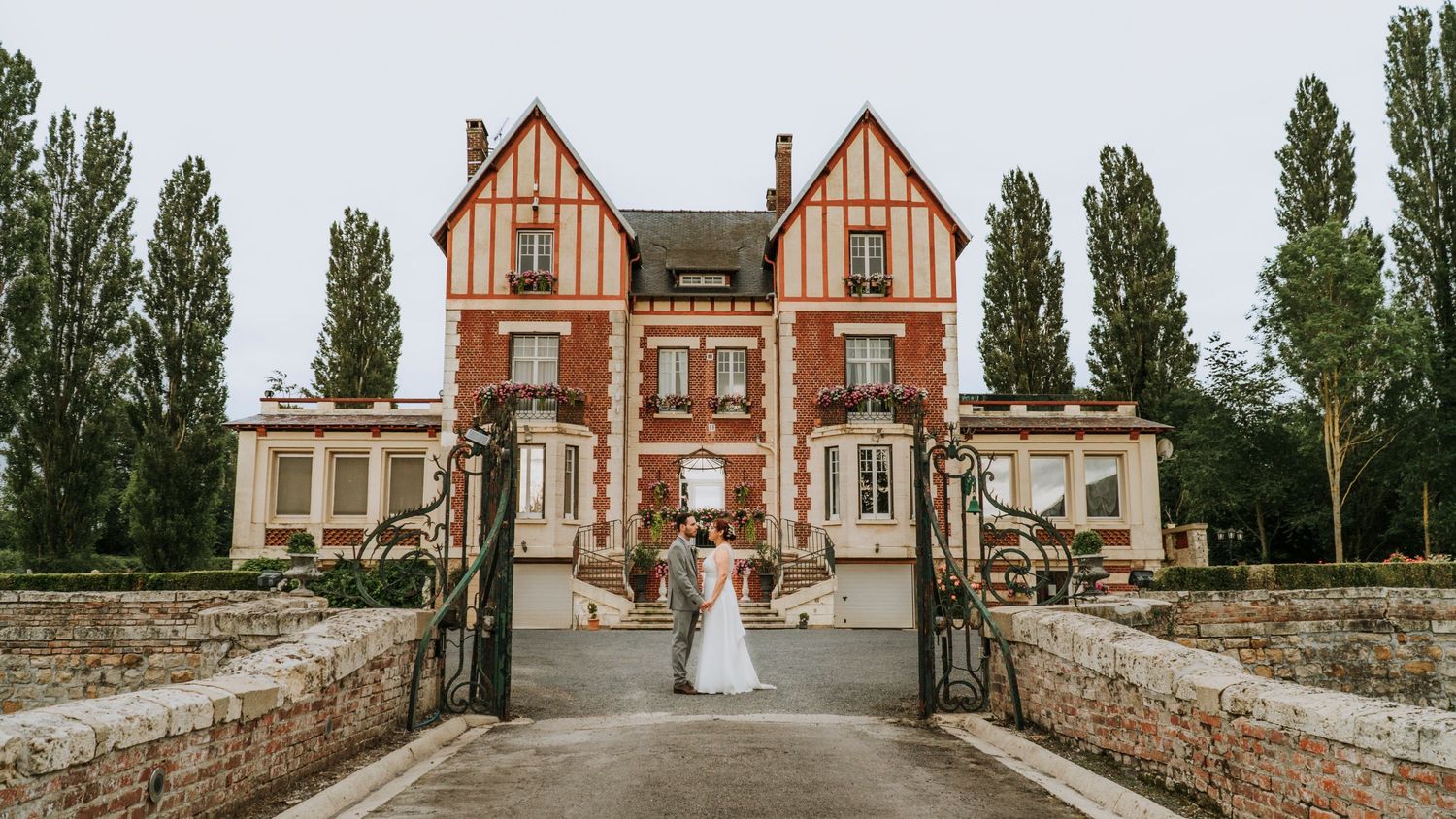 Wide view of a stately Tudor mansion with brick and timber exterior on a cloudy wedding day.