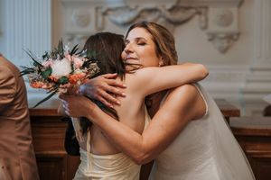 Bride in white gown hugging a guest while holding a floral bouquet at an elegant wedding venue.